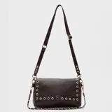 Cartera tipo bandolera de cuero vegano color negro, con solapa decorada con ojetillos metálicos y logo metálico central. Incluye una correa larga ajustable con logo grabado y una cadena decorativa plateada.