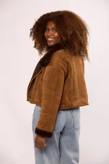 Campera corta tipo gamulán en color negro, con interior y detalles en puños y cuello de corderito sintético al tono. Presenta cierre frontal metálico y un botón decorativo en el ruedo.
