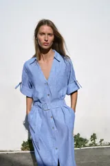 Vestido midi de cuello solapa con escote en pico y mangas tres cuartos ajustables con trabilla. Cuenta con bolsillos delanteros de plastrón, bolsillos laterales ocultos en costura, cierre frontal con botones y cinturón ajustable del mismo tejido con hebilla metálica circular.