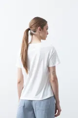 Remera blanca de manga corta con estampado frontal de un florero rojo con rayas verticales y un ramo de flores azules y rojas.