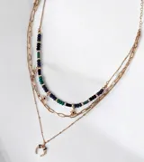 Set de collares tipo cascada en color dorado, compuesto por tres niveles: una gargantilla de cuentas multicolor con dijes de estrellas, una cadena de eslabones y una cadena fina con dije de medialuna.