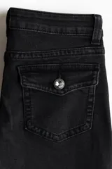 Jean de denim negro elástico, de tiro bajo y corte acampanado desde la rodilla. Cuenta con bolsillos delanteros y bolsillos traseros con solapa y botón.
