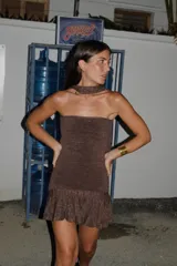 Vestido corto strapless de tejido de punto con acabado brillante, diseño ajustado al cuerpo y falda con volados en el ruedo. Incluye un detalle de cuello tipo gargantilla integrado con una argolla metálica.