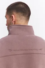 Buzo de algodón con medio cierre frontal y cuello alto. Presenta puños y ruedo acanalados, con un pequeño logo bordado en el pecho.