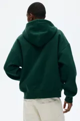 Campera con capucha de tejido pesado de mezcla de algodón con interior cepillado suave. Presenta hombros caídos, capucha forrada con cordón de ajuste, cierre frontal y bolsillos tipo canguro. Cuenta con puños y bajo acanalados, con un corte oversized.