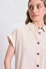 Camisa casual de lino color crudo, con cuello camisero, manga corta doblada y cierre frontal con botones oscuros.