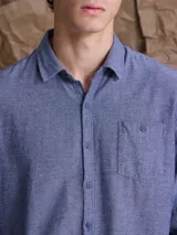Camisa de manga larga en tono azul jaspeado, con cuello clásico, cierre frontal de botones y un bolsillo en el pecho.