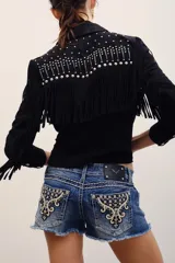 Short de denim azul de tiro bajo, con lavado desgastado, dobladillo desmechado y bolsillos traseros con bordados ornamentales y tachas metálicas.