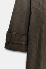 Trench oversize de Zara Woman Collection, confeccionado en mezcla de algodón con estampado de cuadros pequeños. Presenta cuello alto, cierre frontal con botones, mangas largas con trabillas ajustables y bolsillos laterales.