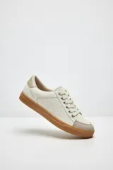 Zapatillas color marfil con detalles dorados en el talón y ojales metálicos. Suela de goma caramelo y cordones beige.