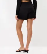Short pollera de bengalina color negro, con diseño cruzado, pretina estructurada y cinturón integrado con hebilla metálica dorada.