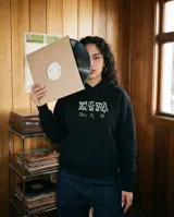 Canguro negro con capucha, de corte regular y ajuste cómodo. Presenta un estampado gráfico en la espalda con la frase 'Cultura de Barrio' en tipografía estilizada y detalles de marca en la parte inferior.