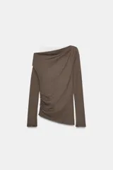 Camiseta de manga larga con diseño asimétrico y efecto de doble capa. Presenta un cuello redondo y un detalle de fruncido lateral que aporta textura y movimiento a la prenda.