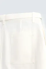 Shorts de algodón color blanco roto, de corte regular fit, con cintura ajustable mediante cinturón del mismo tejido y hebilla metálica. Presenta bolsillos delanteros y bolsillos traseros de vivo.