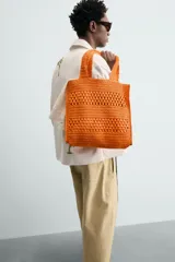 Bolso tipo shopper de color naranja con acabado trenzado y diseño estructurado. Cuenta con compartimento principal y dos asas cortas de mano.