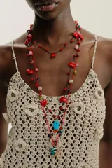 Pack de tres collares de cordones trenzados en tonos rojo y negro, adornados con cuentas de diferentes colores y dijes colgantes: corazones rojos, un dije azul turquesa con forma de pez, un dije azul verdoso con forma de corazón y un dije dorado con textura de concha.