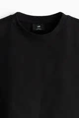 Remera negra de algodón pesado, corte holgado, con cuello redondo ribeteado, hombros caídos y bajo recto.