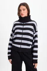 Campera de punto holgada con cuello tipo chomba y cierre frontal oculto. Presenta un diseño de rayas horizontales en tonos marrón, rojo y crema, con puños y ruedo acanalados. Incluye un parche bordado en la manga izquierda.