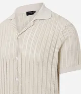 Camisa de manga corta para hombre con cuello solapa y cierre frontal de botones. Presenta un diseño de punto con textura de líneas verticales en color beige y calce regular. Confeccionada en una mezcla de poliéster y algodón sustentable.