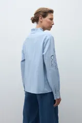 Camisa blanca de manga larga con cuello alto fruncido y bordados calados en el pecho y los hombros.