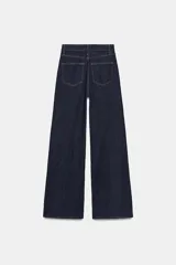 Jeans de tiro alto con corte wide leg y largo completo. Presenta diseño de cinco bolsillos, trabillas en la cintura y cierre frontal con cremallera y botón, con un acabado de efecto lavado.
