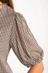 Blusa de algodón con estampado de cuadros vichy en tonos negro y blanco. Presenta escote en V, cierre frontal con botones y mangas cortas abullonadas con terminación elástica.