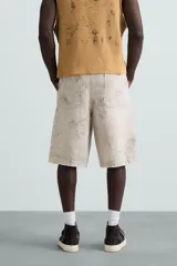 Bermuda de algodón color beige claro con efecto lavado y estampado abstracto en tonos grises. Diseño de corte relajado con cierre frontal de botón y cremallera, bolsillos delanteros y bolsillos traseros de plastrón.