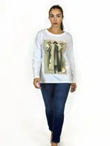 Remera blanca de manga larga con cuello redondo y corte recto. Presenta un estampado frontal artístico que representa figuras estilizadas con sombreros en tonos tierra y detalles en dorado.
