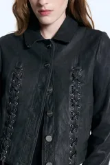 Campera de cuero merino negro con diseño de tientos entrelazados en el frente y la espalda, cierre frontal con botones metálicos y corte entallado.