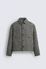 Sobrecamisa de corte relajado con textura de tejido estructurado en color gris y negro. Presenta cuello clásico, cierre frontal con botones, mangas largas con puños abotonados y bolsillos de plastrón en el pecho.