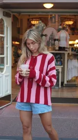 Cárdigan con rayas verticales rojas y rosadas, cuello polo y cierre frontal con botones.