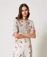 Top de tejido calado color crema con estampado floral en tonos lila, naranja y verde. Tiene cuello redondo y mangas cortas.