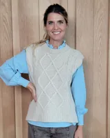 Chaleco de punto en color beige, con diseño de trenzas y rombos en el frente, cuello redondo y terminaciones en rib.