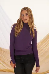 Polera negra de cuello alto y mangas largas con detalle de botones plateados en los puños.