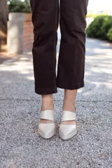 Zapato de cuero color beige, con punta fina, tira sobre el empeine y pulsera con hebilla al tobillo. Tiene talón descubierto y taco cuadrado.