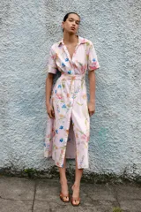 Vestido midi de corte camisero con estampado floral multicolor sobre fondo rosa claro. Presenta cuello solapa, manga corta, cierre frontal con botones y cinturón del mismo tejido con hebilla forrada.