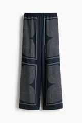Pantalón de tiro alto color azul marino, confeccionado en tela con leve brillo, con cintura elástica y diseño de piernas rectas con estampado geométrico de líneas claras.