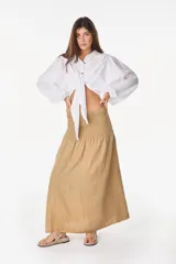 Top blanco de manga larga con diseño abullonado, cuello camisero, cierre frontal con botones y nudo ajustable en la cintura. Con textura sutil en la tela.
