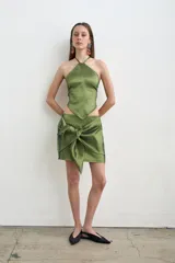Falda corta verde oliva confeccionada en tafeta, con diseño cruzado y un gran moño anudado en el frente.
