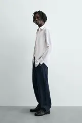 Camisa de manga larga, color blanco, con cuello italiano y corte slim fit. Presenta cierre frontal de botonadura y puños con botón.