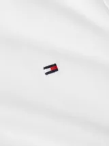 Chomba blanca de manga corta con corte slim, confeccionada en piqué de algodón y elastano. Presenta cuello con ribete tricolor (rojo, blanco y azul marino) y cartera de dos botones. Posee el logo de Tommy Hilfiger bordado en el pecho.