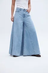 Jean de mezclilla celeste claro, tiro medio, con corte extremadamente ancho y acampanado desde la cadera hasta el bajo, con costuras verticales que acentúan la amplitud de la pierna.