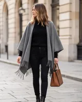 Poncho de abrigo color gris con flecos en el borde inferior y diseño envolvente.