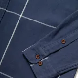 Camisa de franela azul con diseño a cuadros blancos, de manga larga, con cuello clásico, cierre frontal con botones, dos bolsillos con solapa abotonada en el pecho y corte recto.