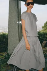 Vestido midi de Zara Woman Collection confeccionado en hilatura con lino, color gris. Presenta cuello redondo, manga corta caída, detalle de frunces y lazadas laterales en el mismo tejido, y cierre en la espalda.