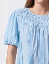 Blusa blanca de gasa marca Zac & Rachel, con frunces en la parte delantera, mangas cortas con puño elastizado, abertura central en la espalda y botón.