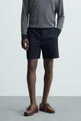 Bermuda de hombre color beige claro, corte regular fit, con pliegues frontales, bolsillos delanteros y bolsillos traseros de doble vivo con botón.