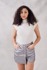 Top sin mangas, cuello tortuga, color blanco con acabado brillante o metálico. Tejido acanalado y ajustado al cuerpo.