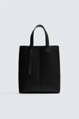 Bolso tipo shopper de diseño minimalista en color negro, con estructura vertical, doble asa de hombro y detalle de tira decorativa frontal con cierre magnético.