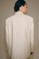 Blazer de Zara Woman Collection confeccionado en mezcla con lino, color beige con diseño de rayas finas verticales. Presenta cuello solapa, manga larga, bolsillos de parche en el delantero y cierre frontal con botones oscuros a contraste.